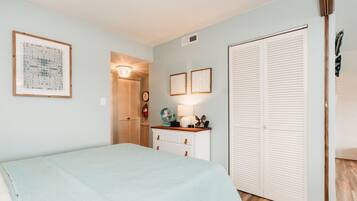 A bedroom with a bed, a dresser, a nightstand, a fan, and a closet.