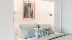 Una cama bien hecha con una colcha azul claro y almohadas, una obra de arte abstracta enmarcada encima, y un armario blanco con una puerta azul claro.