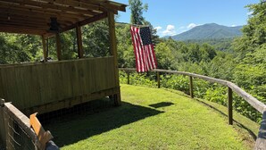 En paviljong av trä med en amerikansk flagga, omgiven av en gräsyta och med utsikt över berg.