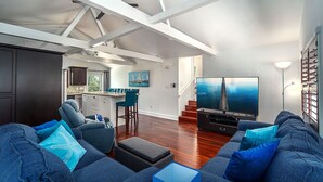 A modern living room with a large TV, dark wood flooring, and a blue sofa set. - Captain House (Summerland Key)