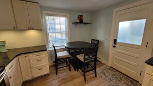 A kitchen with a dining table, chairs, cabinets, a window with blinds, a coffee maker, and a rug. - Historic Newport...steps to downtown/wharfs dining, shopping, attractions (Newport)