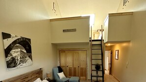 A bedroom with a large bed, a chair, a ladder, and a door leading to a loft area. - Steps to Sherburne Base Lodge and Lift at Burke Mountain (Burke)
