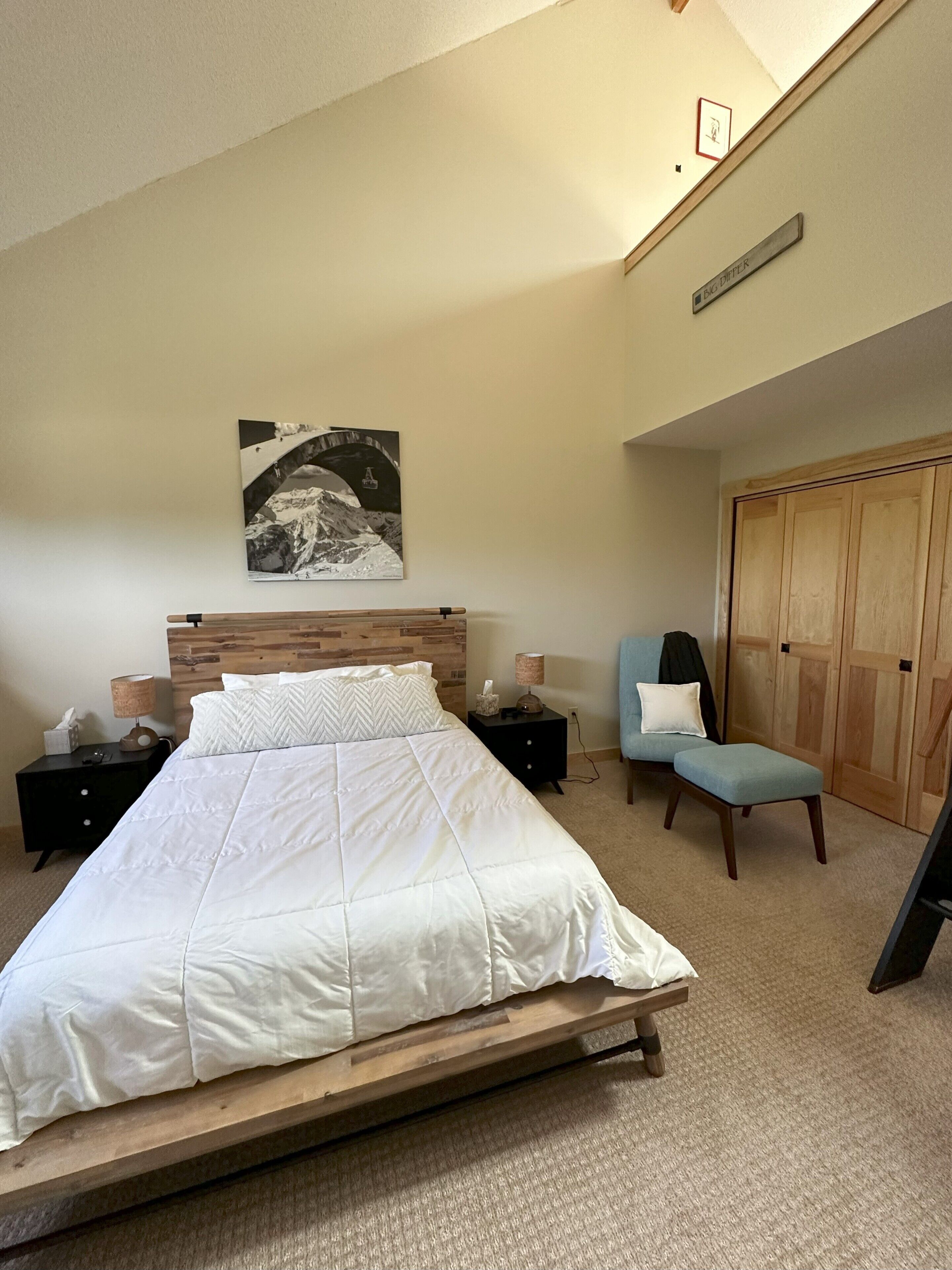 A bedroom with a large bed, a nightstand, a chair, a wardrobe, and a picture on the wall.