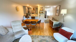 A modern living room with a sofa, a coffee table, a dining area with chairs, a kitchen in the background, and a small side table with a lamp. - Steps to Sherburne Base Lodge and Lift at Burke Mountain (Burke)
