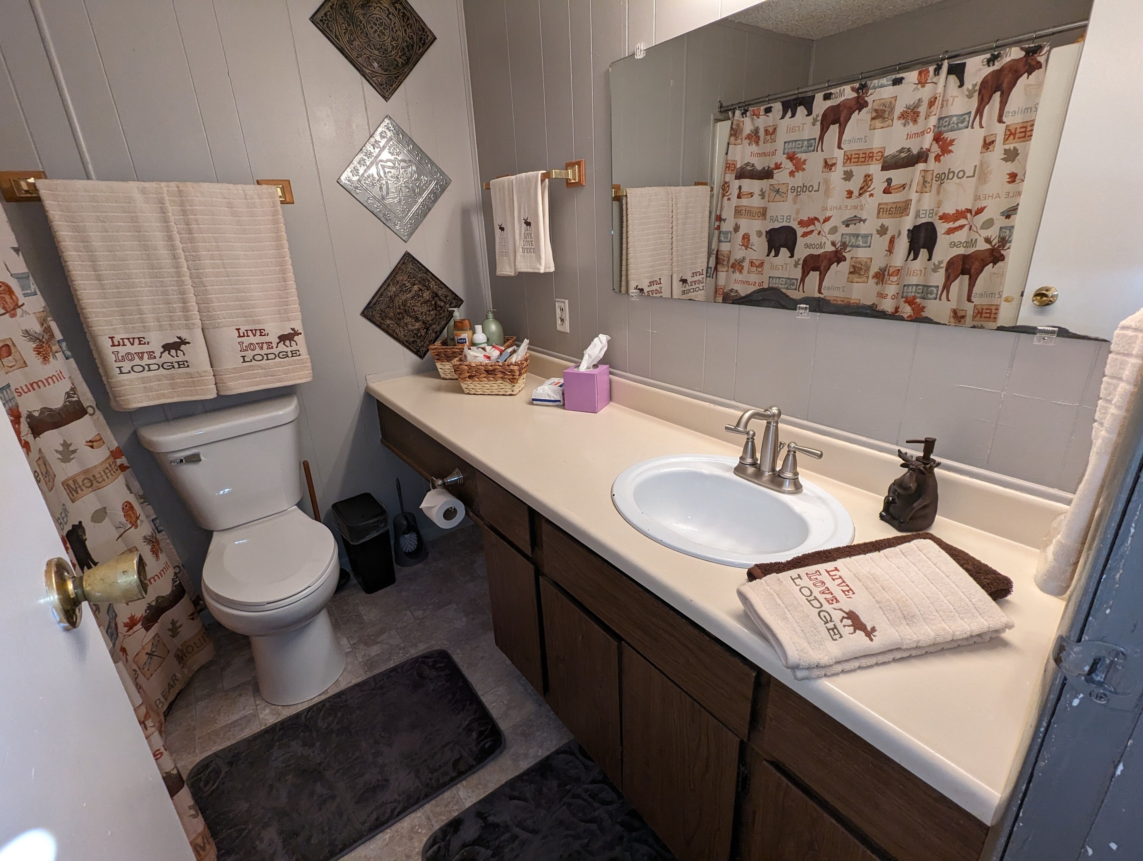 A bathroom with a toilet, sink, and mirror. There are towels with 'Live. Love. Lodge.' printed on them.