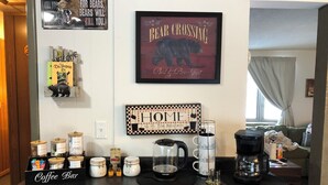 A kitchen counter with a coffee bar, jars of tea and sweeteners, a coffee maker, and a mug.