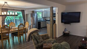 A living room with a dining area, a sofa, a TV, and a kitchen in the background.