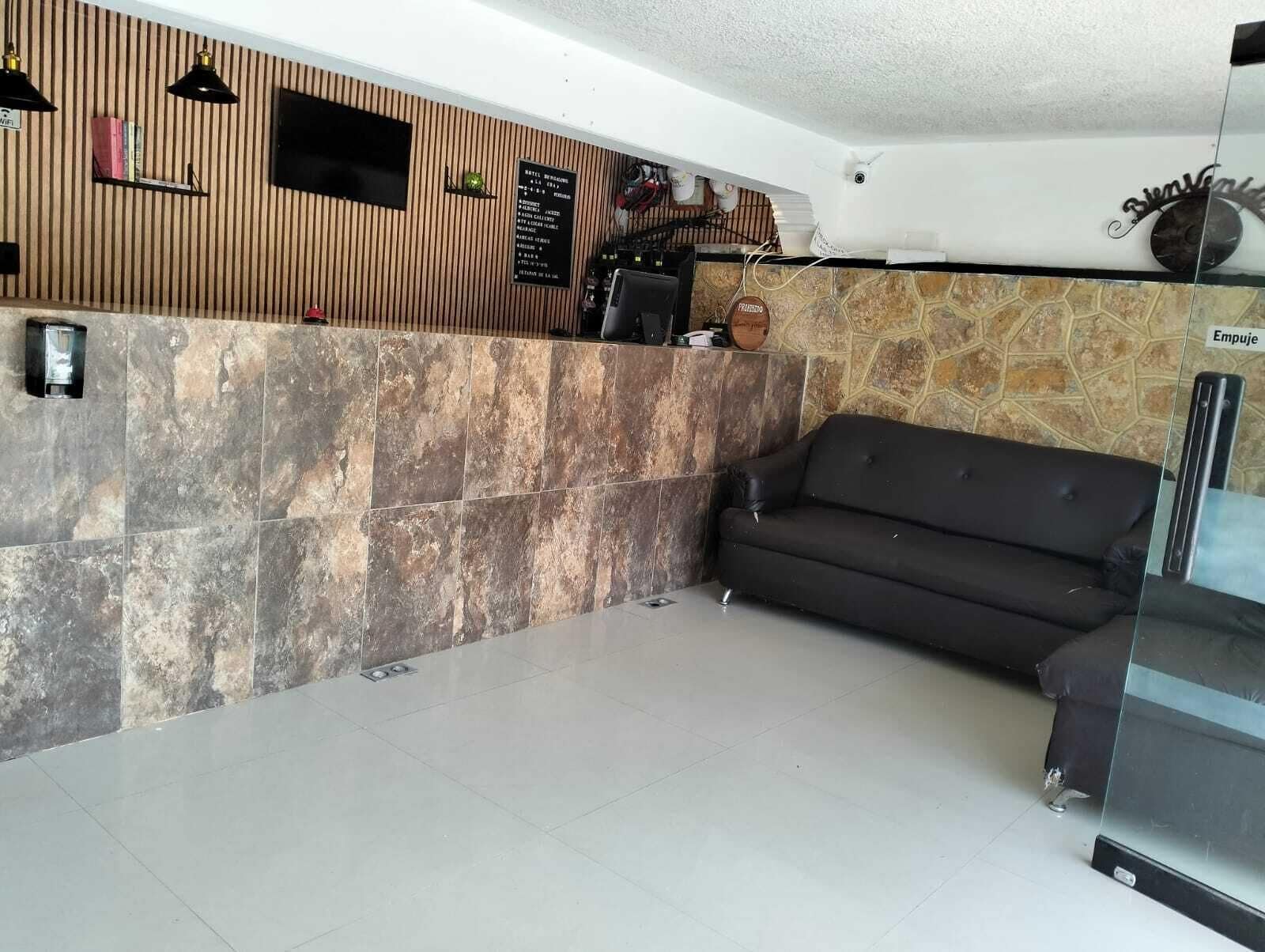 En reception med væg af træpaneler, en stenvæg, en sort lædersofa og en glasvæg.