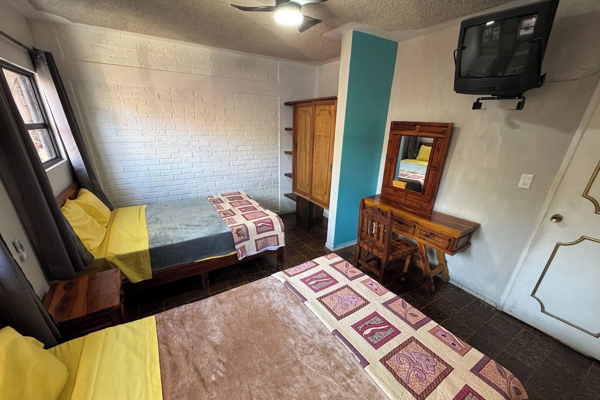 Ein Zimmer mit zwei Betten, einem Holztisch, einem Spiegel und einem Fernseher.