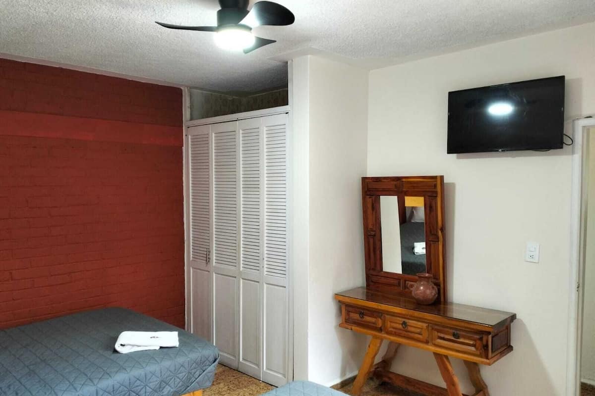 Ein Schlafzimmer mit zwei Betten, einer Holzkommode, einem Spiegel, einem Deckenventilator und einem Fernseher.