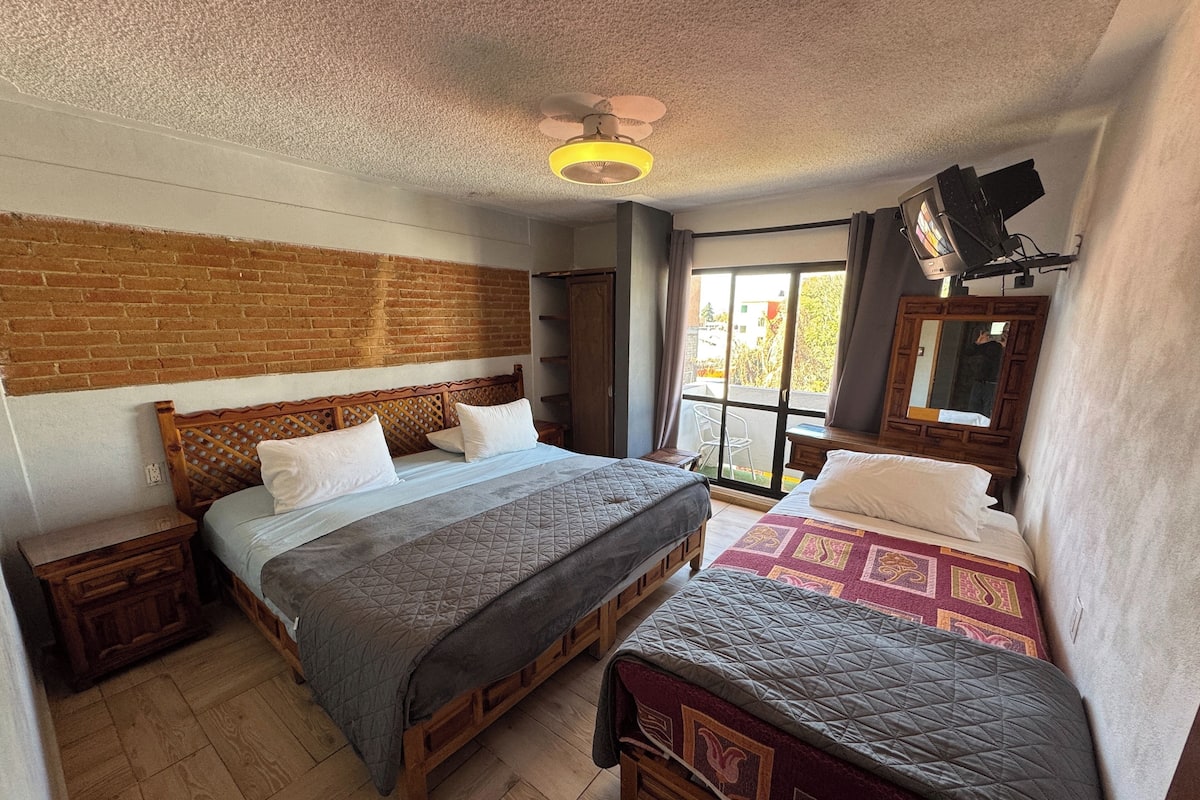 Ein Zimmer mit zwei Betten, einer Ziegelwand, einem Holz-Kopfteil, einem Deckenventilator und einem Fenster mit Blick.