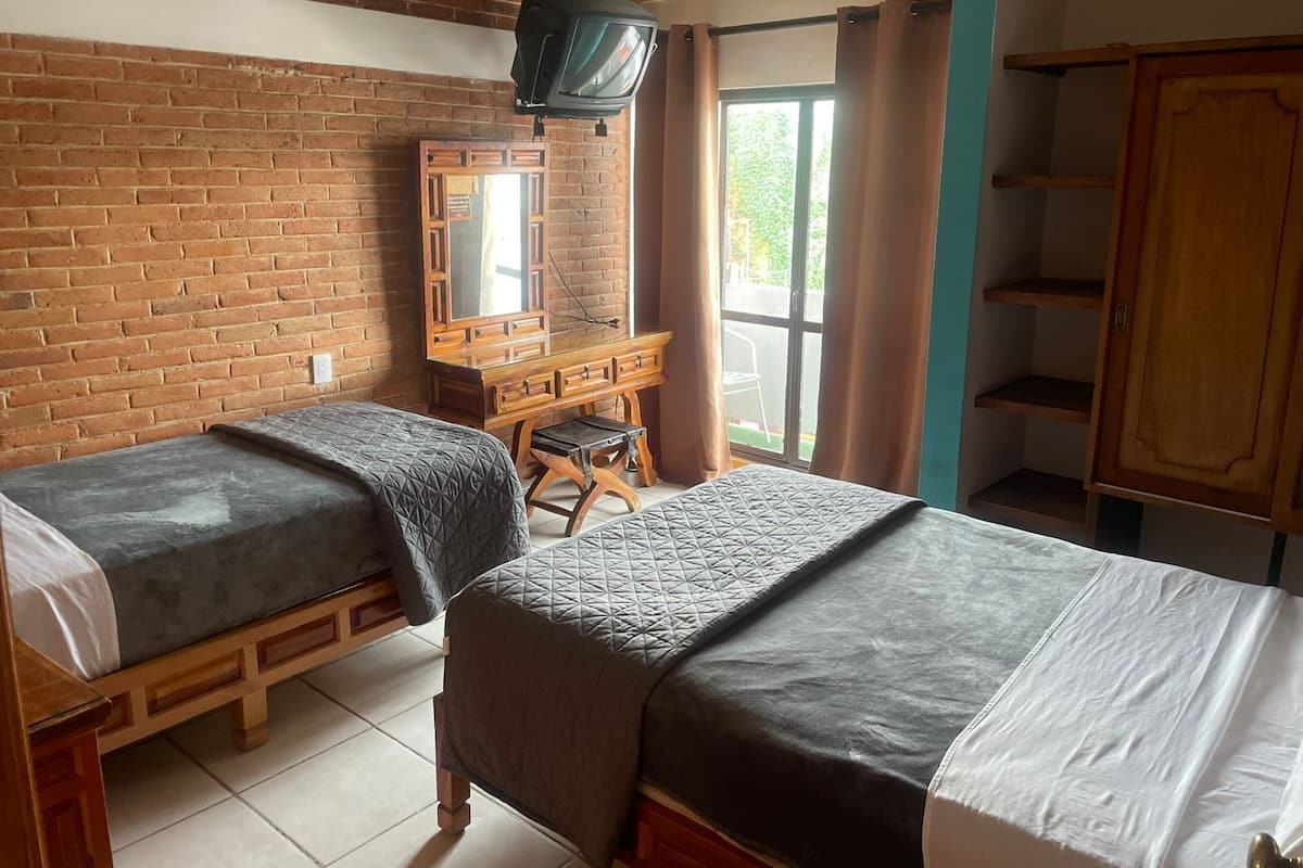 Ein Zimmer mit zwei Einzelbetten, einem Holzschrank, einem Fernseher und einem Fenster mit Vorhängen.