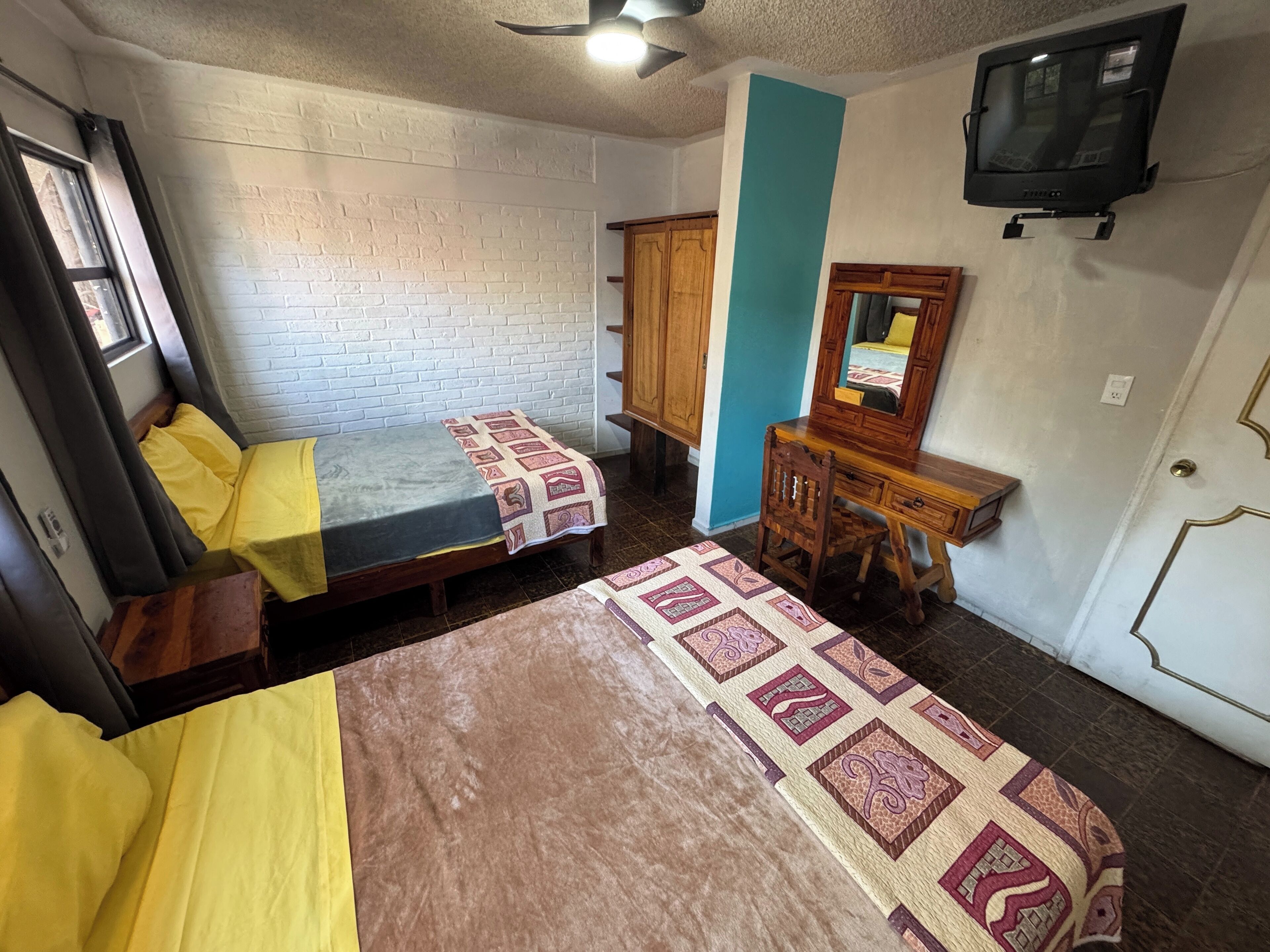 Una habitación pequeña y acogedora con dos camas individuales, un escritorio de madera, un espejo y un televisor.