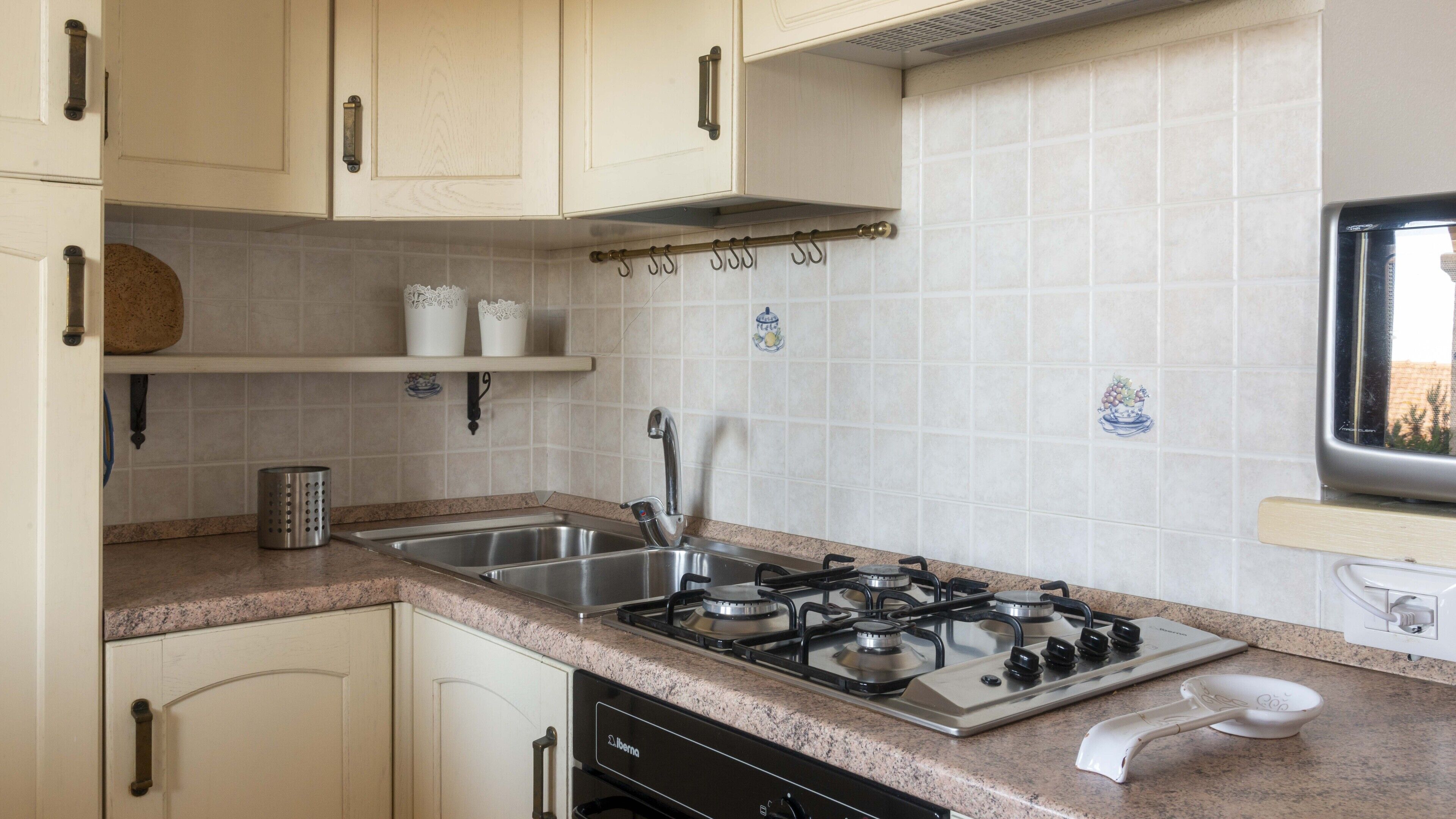 Una cocina con estufa a gas, pileta de acero inoxidable y alacenas de color claro.