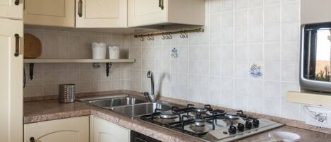Una cocina con estufa a gas, pileta de acero inoxidable y alacenas de color claro.