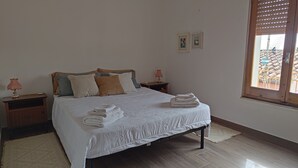 A neatly made bed with folded towels, a wooden headboard, two bedside tables with lamps, and a window with blinds.