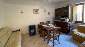 A dining area with a wooden table set for four, a blue air conditioner, and a kitchen area with a microwave and cabinets.