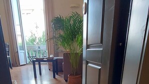Een hotelentree met een deurmat waarop staat 'Mi casa es tu casa', een potplant en een uitzicht op het buitengebied door de geopende deur.