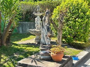 Un jardin orné d’une statue représentant une femme et un enfant, d’un abreuvoir à oiseaux et d’une plante en pot.