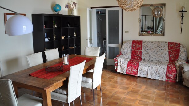 Un comedor con una mesa de madera, sillas blancas, un mantel individual rojo y un globo terráqueo en un estante.