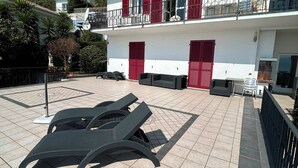 Un edificio con patio de baldosas, contraventanas rojas y mobiliario exterior.