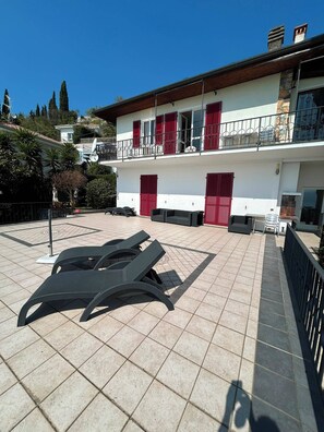 Ein Gebäude mit einer gefliesten Terrasse, roten Fensterläden und Gartenmöbeln.