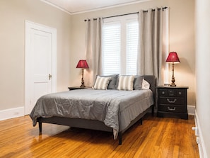 A bedroom with a bed, two bedside tables, a door, and a window with curtains. - On Park house! 9 miles to base! (Columbus)
