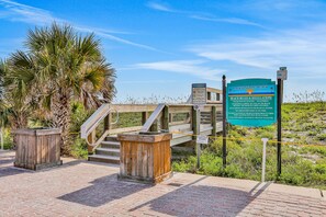 Enjoy the beachfront views from this picturesque spot, where a wooden staircase leads down to the sand, surrounded by palm trees and a clear sky.