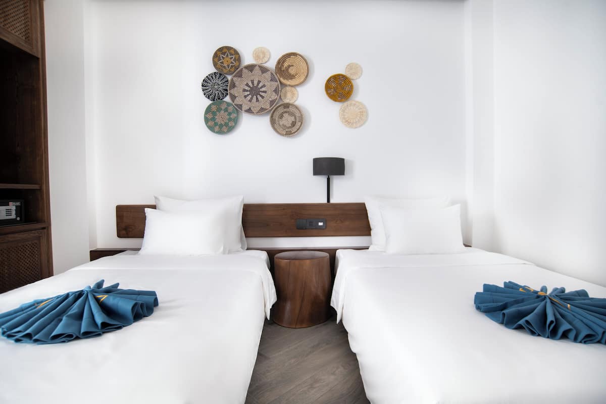 A hotel room with two beds, a wooden headboard, a wall art piece, a bedside table, and a lamp.