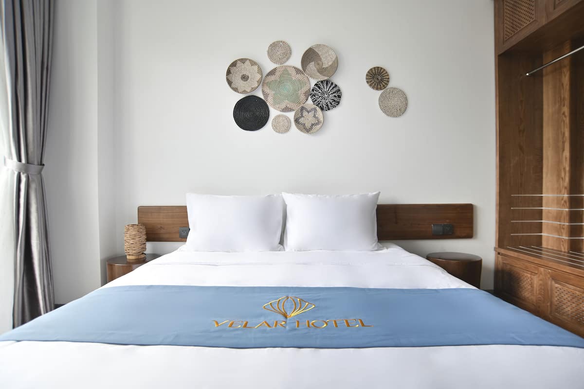 A hotel room with a bed, white pillows, a blue bedspread, and a wall decoration.