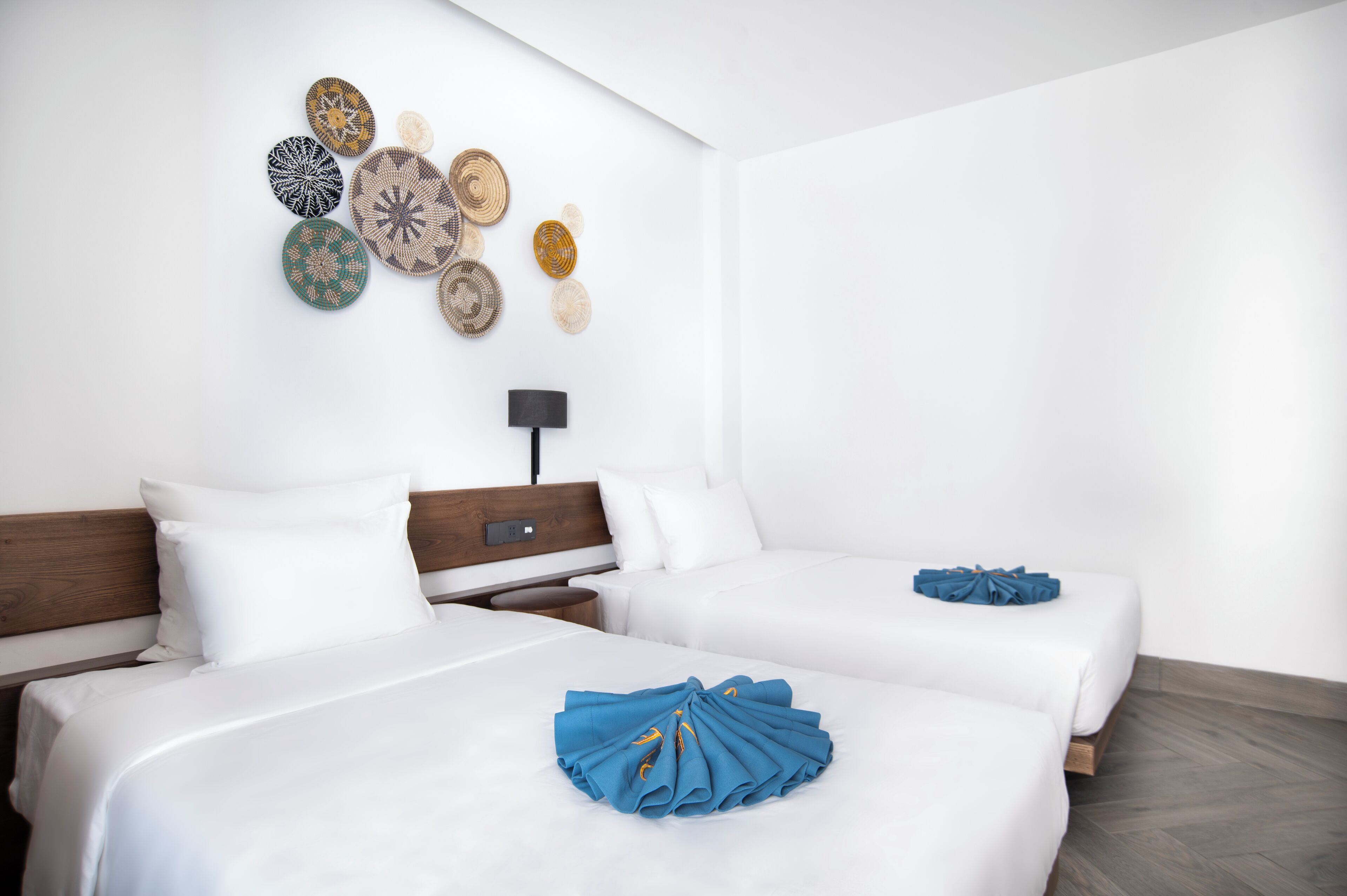 A hotel room with two beds, a nightstand, a lamp, and decorative wall art.
