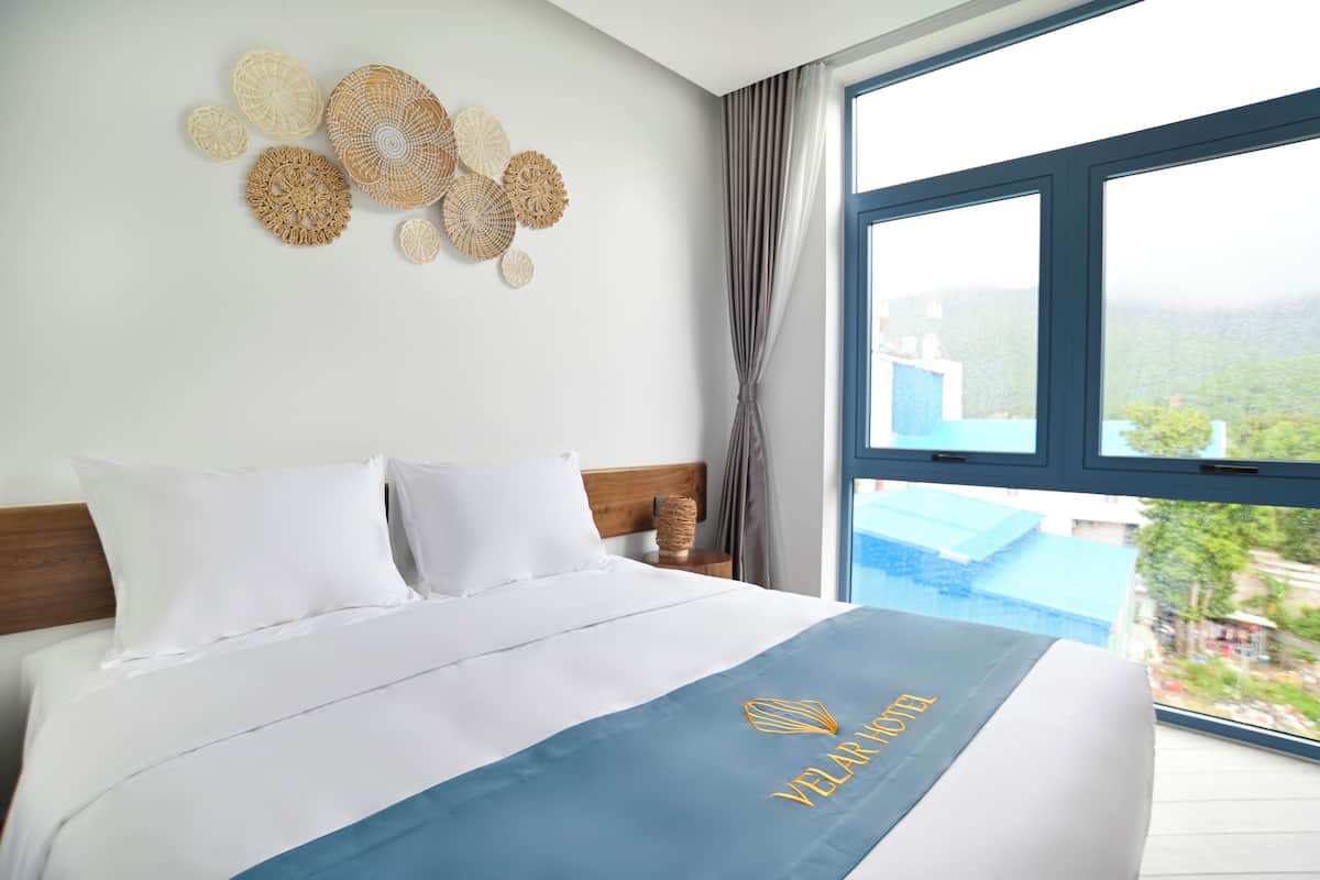 A hotel room with a bed, a view of the outside, and a wall with woven decorations.