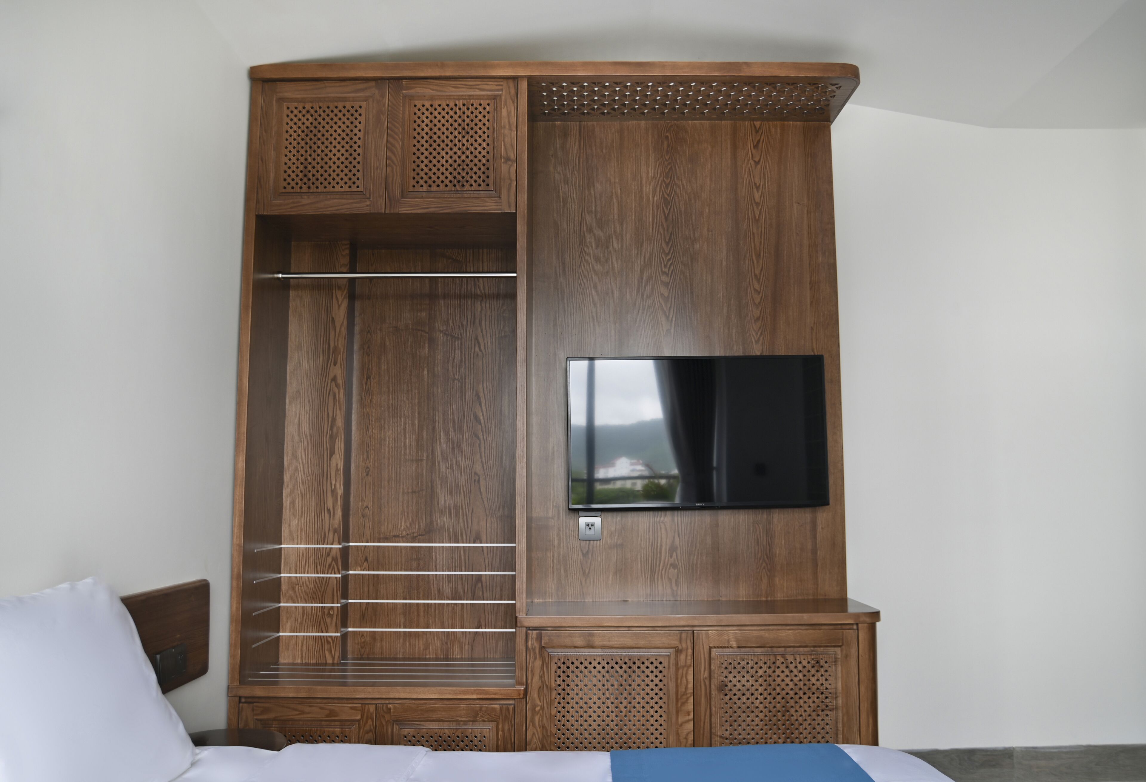 A wooden wardrobe with a television mounted on the wall, a hanging rod, and a lower cabinet.