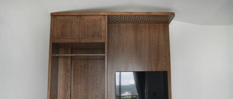 A wooden wardrobe with a television mounted on the wall, a hanging rod, and a lower cabinet.