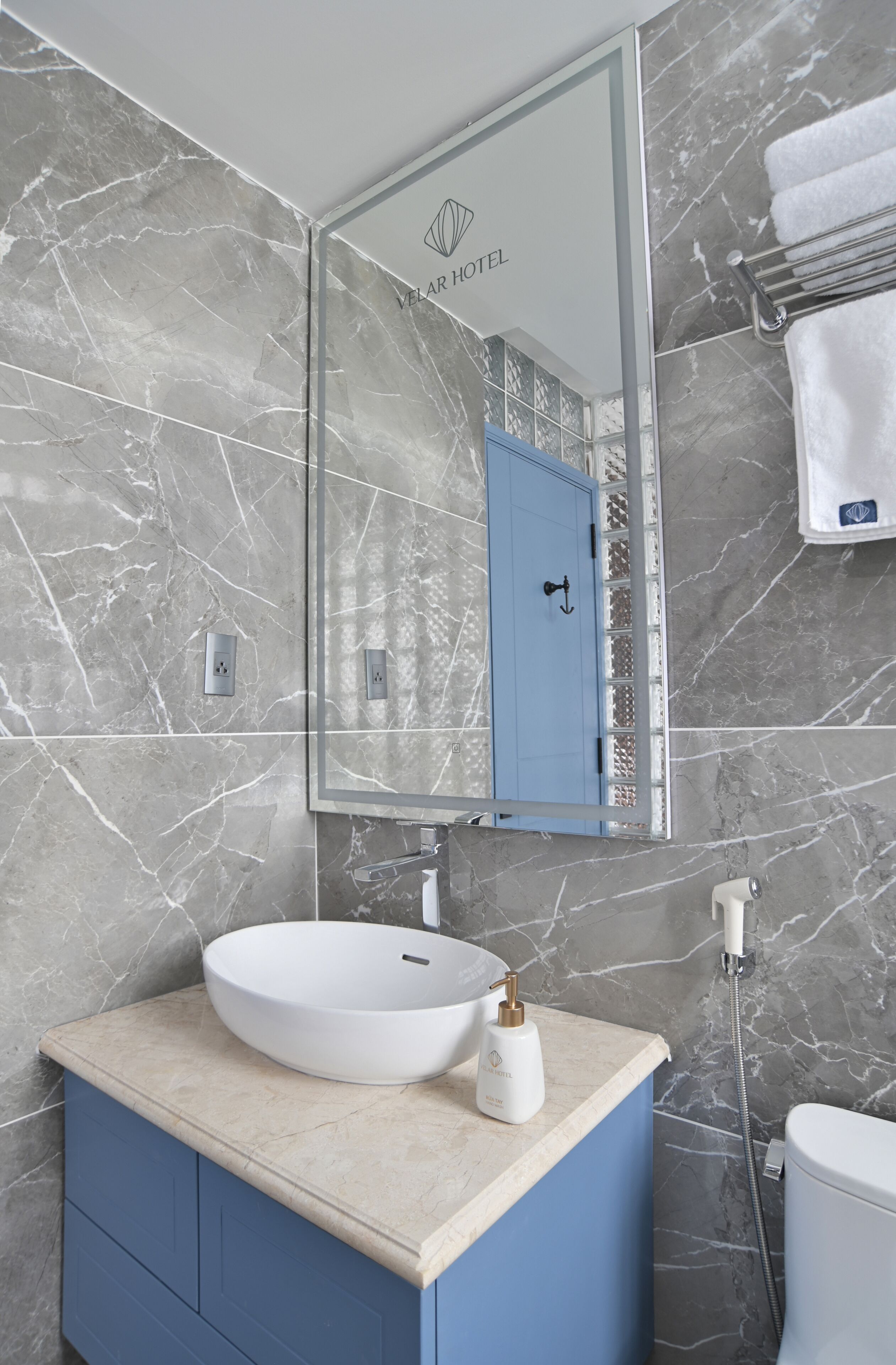 Un baño con pared de mármol, una puerta azul, un lavamanos blanco y un perchero.