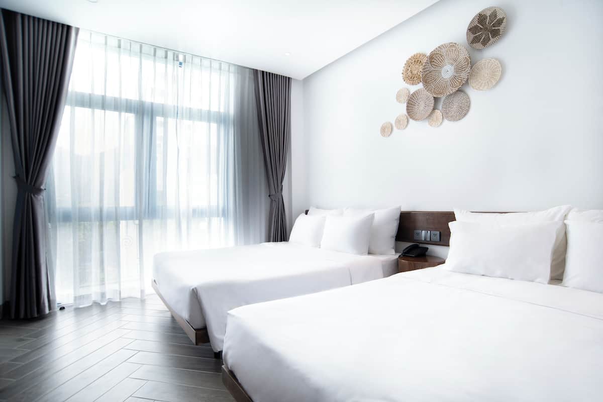 A hotel room with two beds, a large window with curtains, and a wall with decorative plates.