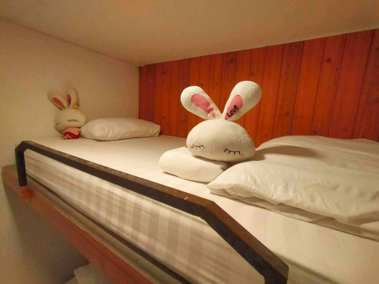 Una cama con un almohadón blanco, un conejo de peluche y un peluche más pequeño.