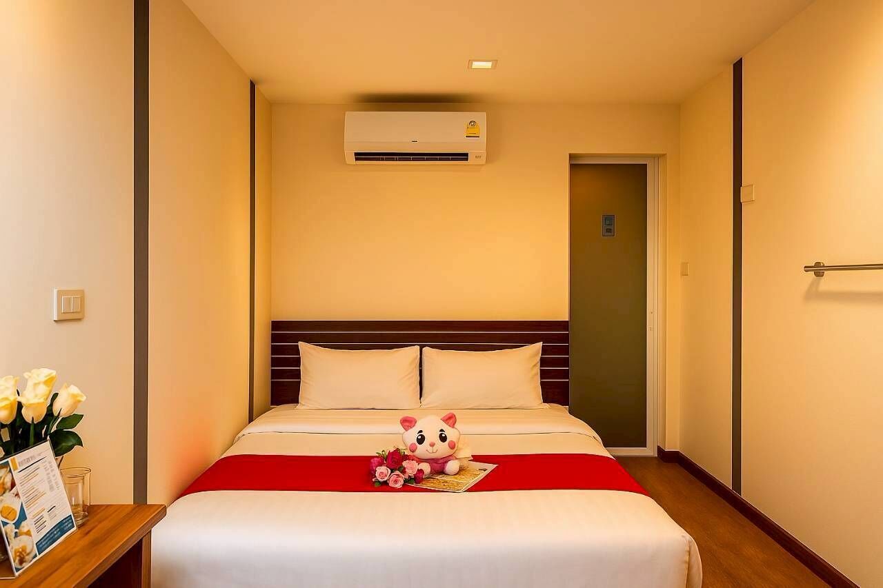 A hotel room with a bed, a plush toy, a vase of flowers, and an air conditioning unit.