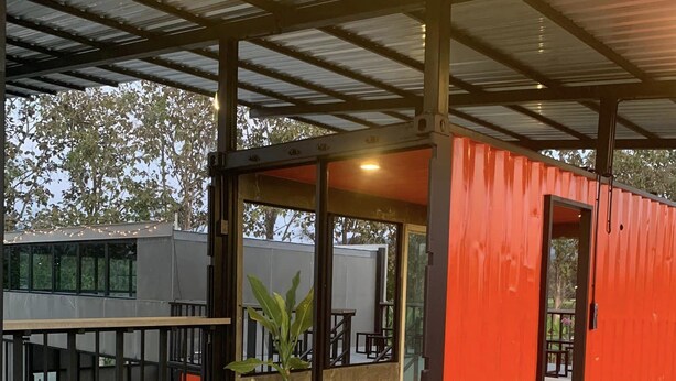 Un patio exterior con zona de estar techada, con mesas y sillas, y vistas al edificio contiguo.