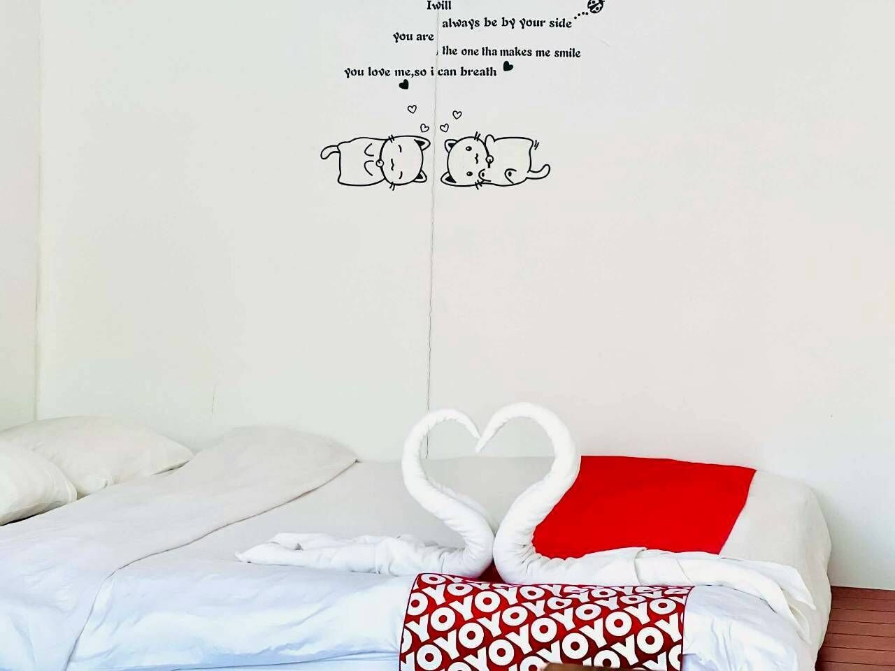 Una cama con ropa de cama blanca, un almohadón rojo y una decoración de toalla con forma de corazón.