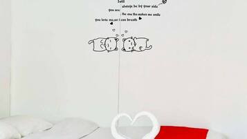 Una cama con ropa de cama blanca, un almohadón rojo y una decoración de toalla con forma de corazón.