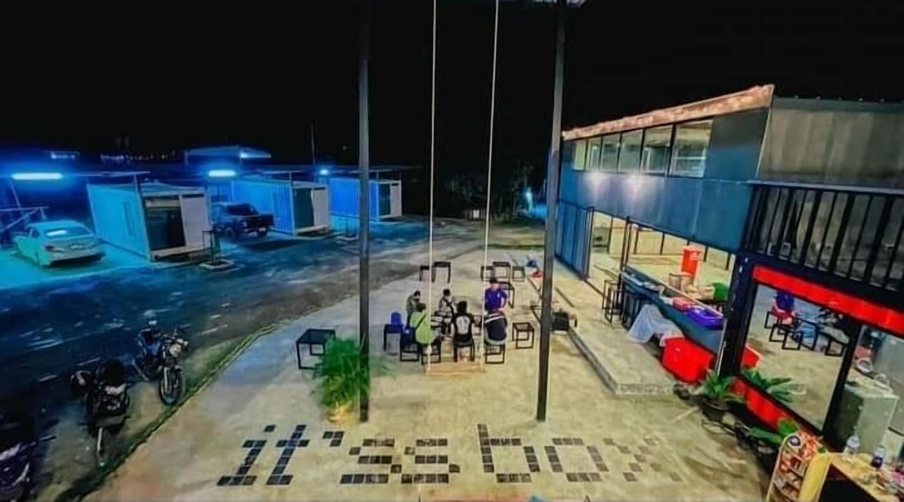 Un estacionamiento con un edificio que tiene un amplio frente de vidrio y mesas al aire libre.