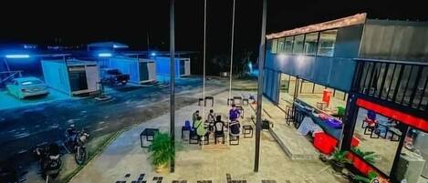 Un estacionamiento con un edificio que tiene un amplio frente de vidrio y mesas al aire libre.