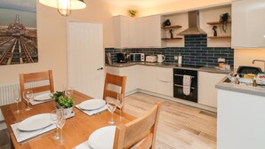 Une cuisine moderne avec des meubles blancs, un dosseret en carreaux noirs et un coin repas avec une table en bois, mise pour quatre personnes.