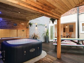 A hot tub under a wooden pergola, a dining area with a table and chairs, and a brick wall with a white door. - 10 Walton Terrace (Guisborough)