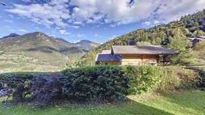 Una baita di legno con tetto spiovente, immersa nel verde e con montagne sullo sfondo.