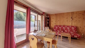 Zona pranzo con tavolo di legno apparecchiato per quattro persone, un divano rosso con motivo decorativo e una libreria in legno.