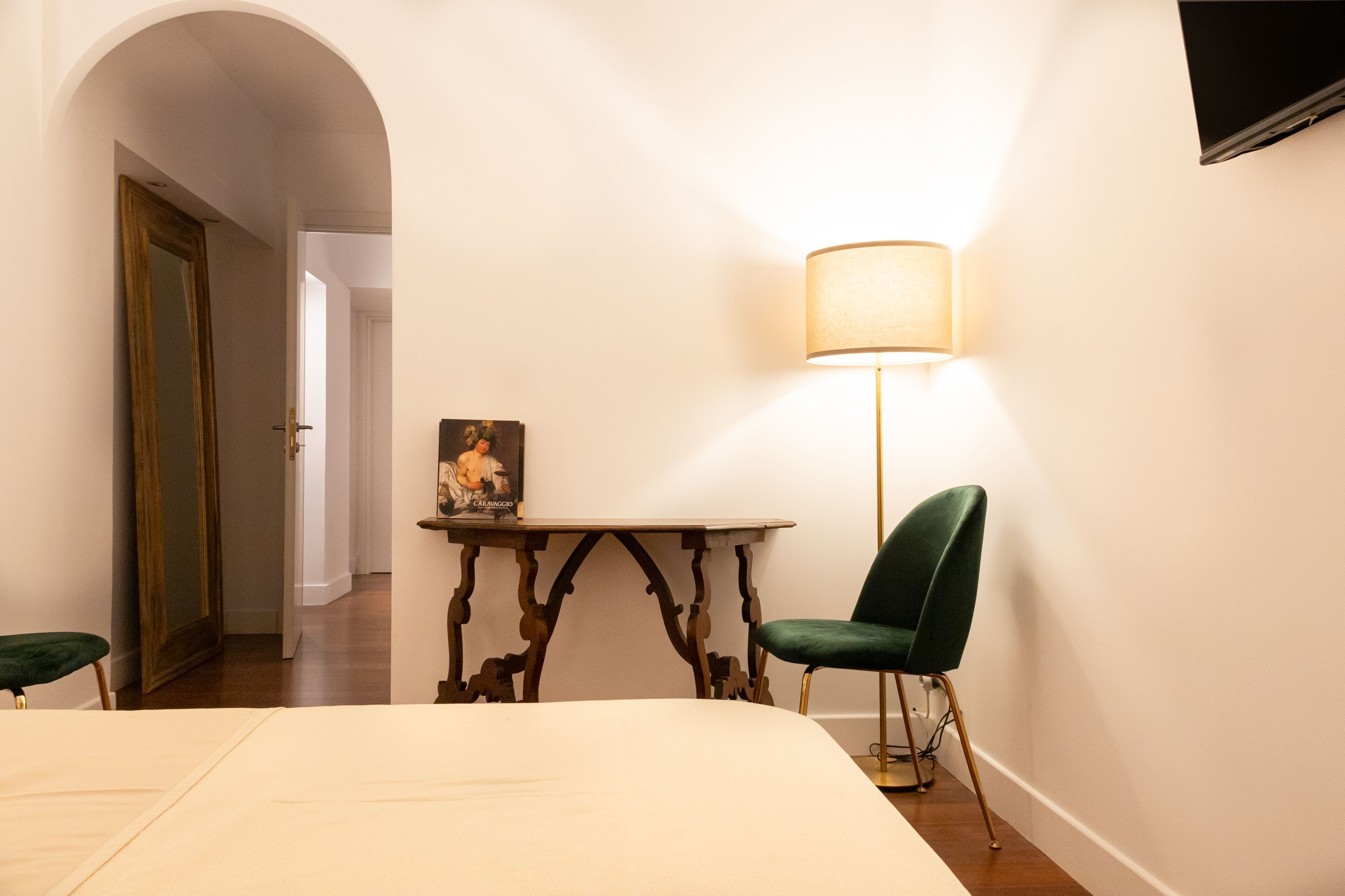 Habitación de hotel con cama, escritorio con lámpara, silla y televisor montado en la pared.