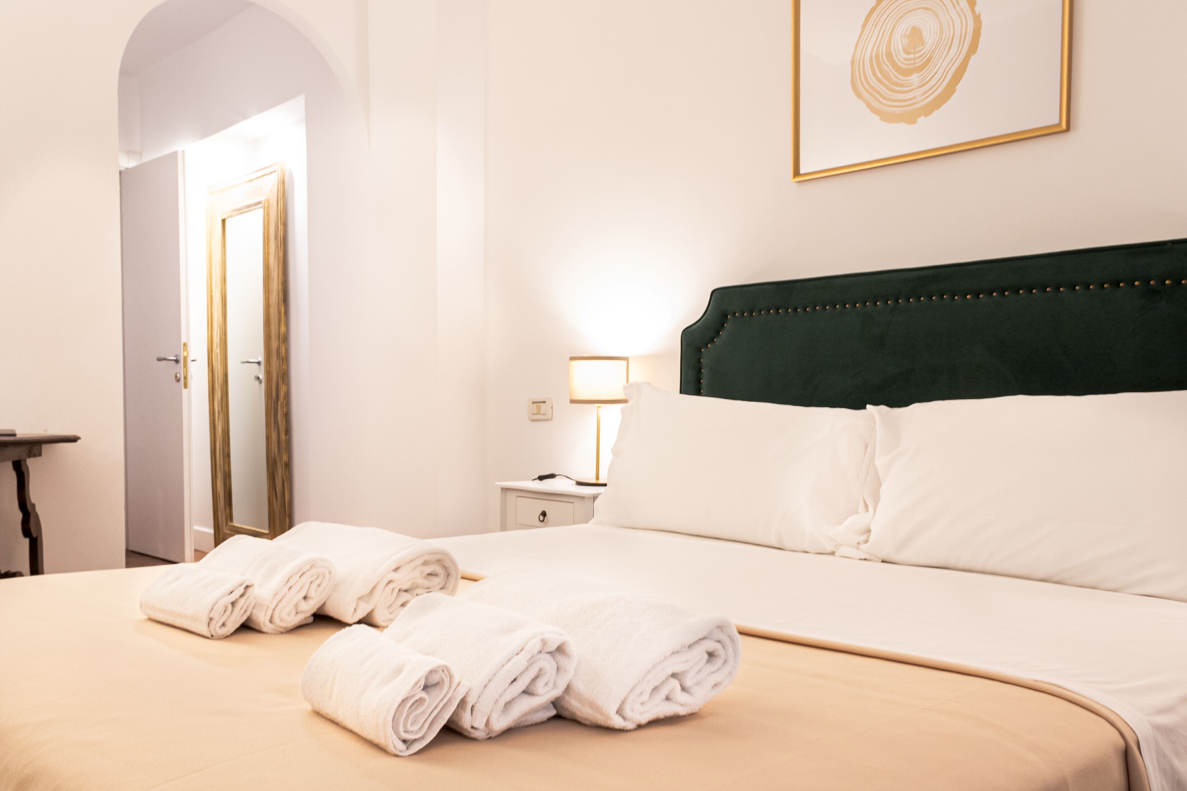 Una cama bien hecha con toallas blancas enrolladas, una lámpara de noche y una obra enmarcada en la pared.