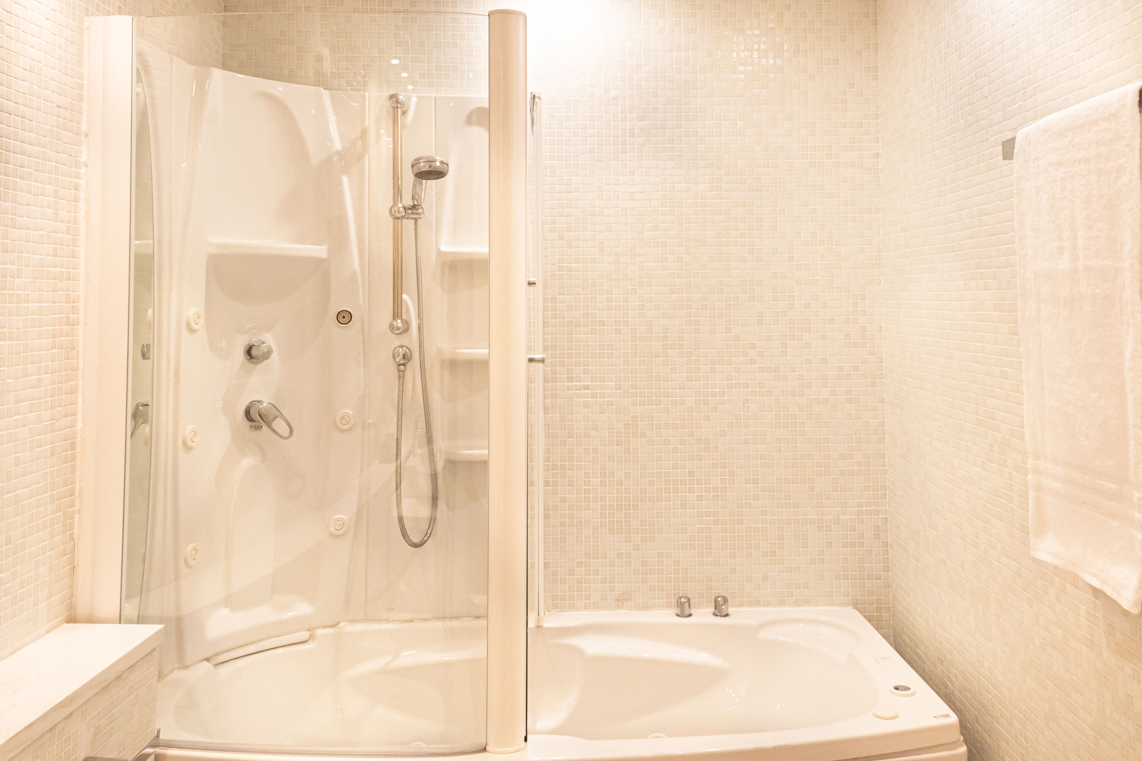 Eine begehbare Dusche mit Glastür, eine Badewanne und eine mit Fliesen verkleidete Wand.